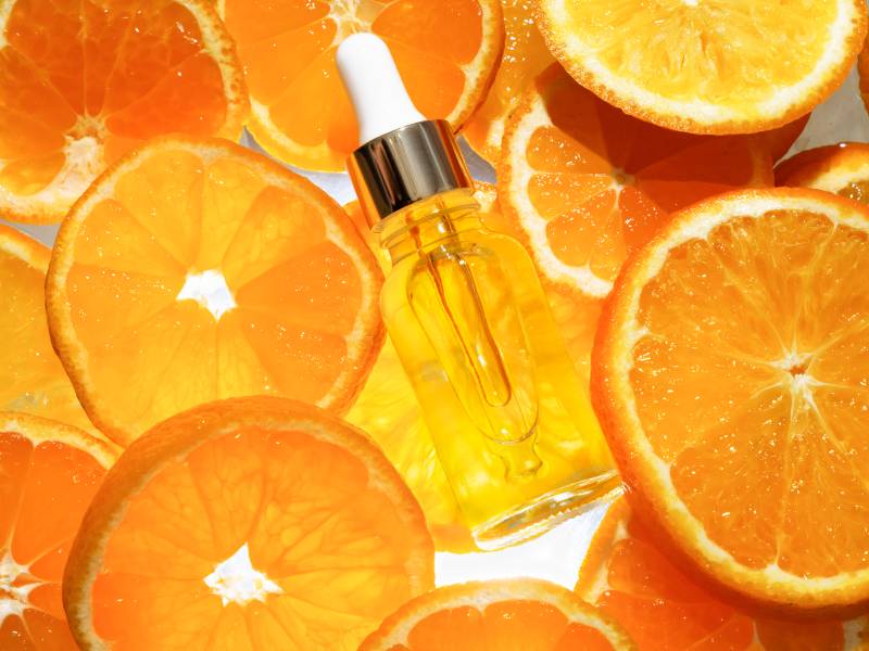 A bottle of orange oil surrounded by sliced oranges.