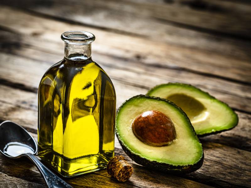 A bottle of oil and two halves of an avocado.