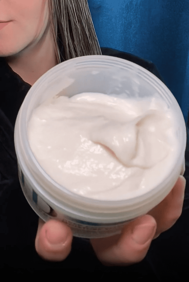 Person holding a container of white cream.