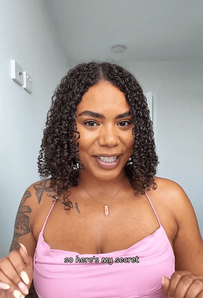 Smiling woman with curly hair, pink top.