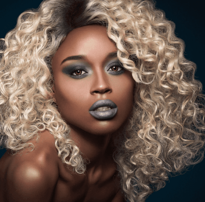 Blonde curly-haired person with dramatic makeup.